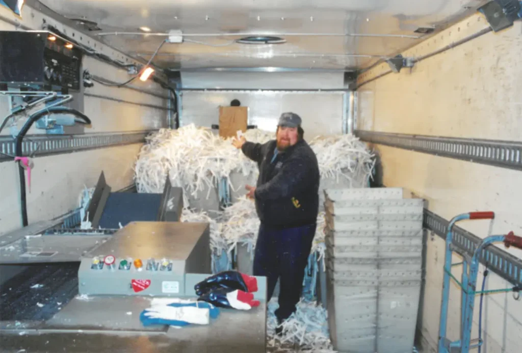 Historical photo of Country Mile Document Destruction owner standing among piles of shredded paper inside his traveling shredder truck - 1